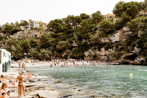 People enjoying a beach day at a scenic coastal location with trees and buildings in the background.